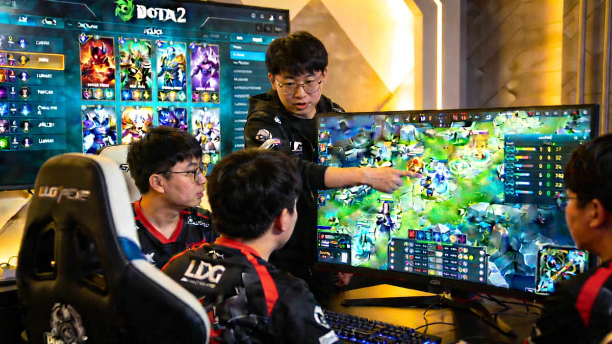 LGD战队教练xiao8在选手身后进行战术指导，大屏幕显示DOTA2英雄选择界面与数据面板