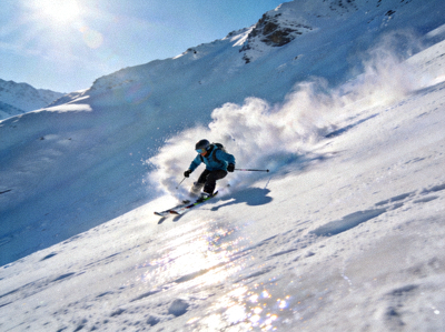 滑雪运动员从雪山坡道高速滑下，身后扬起飞扬雪雾