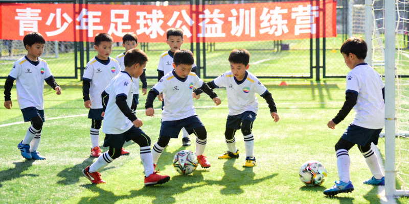 青少年体育公益活动现场，小球员在绿茵场上进行足球训练
